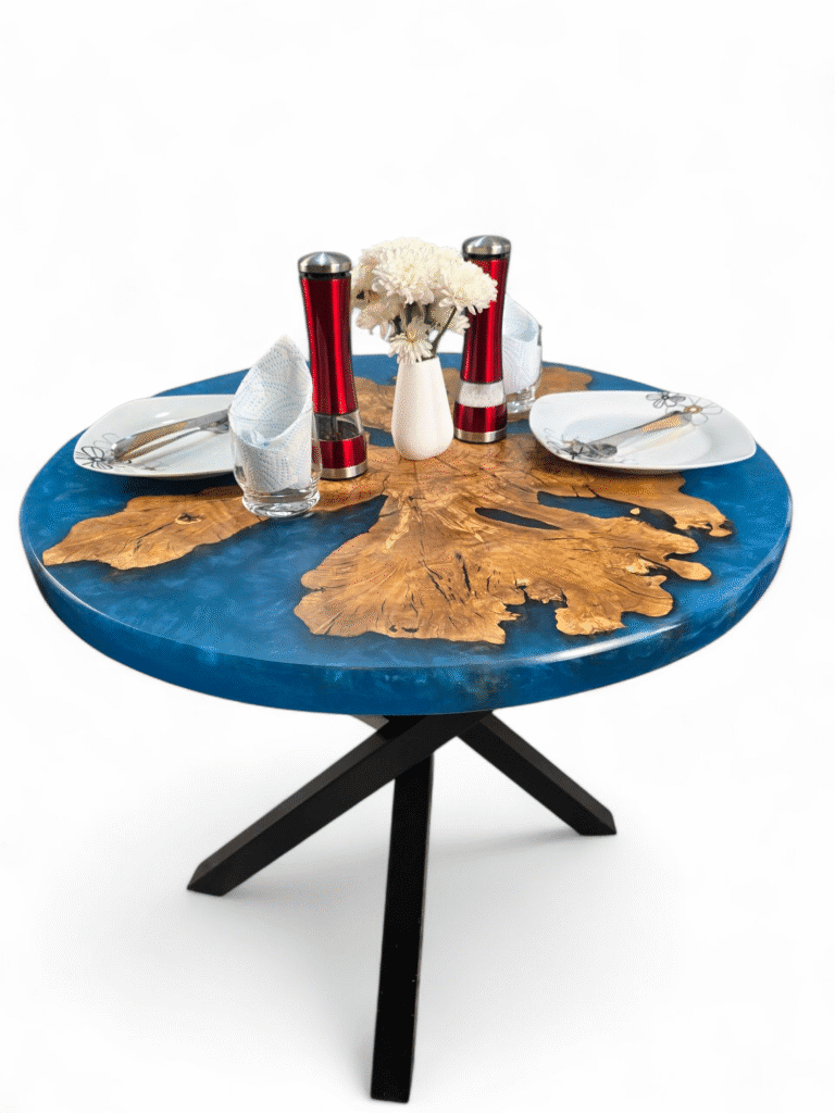 A modern round table with a vibrant blue, swirling epoxy resin surface encasing a uniquely shaped piece of light wood that suggests the branches and trunk of an olive tree.