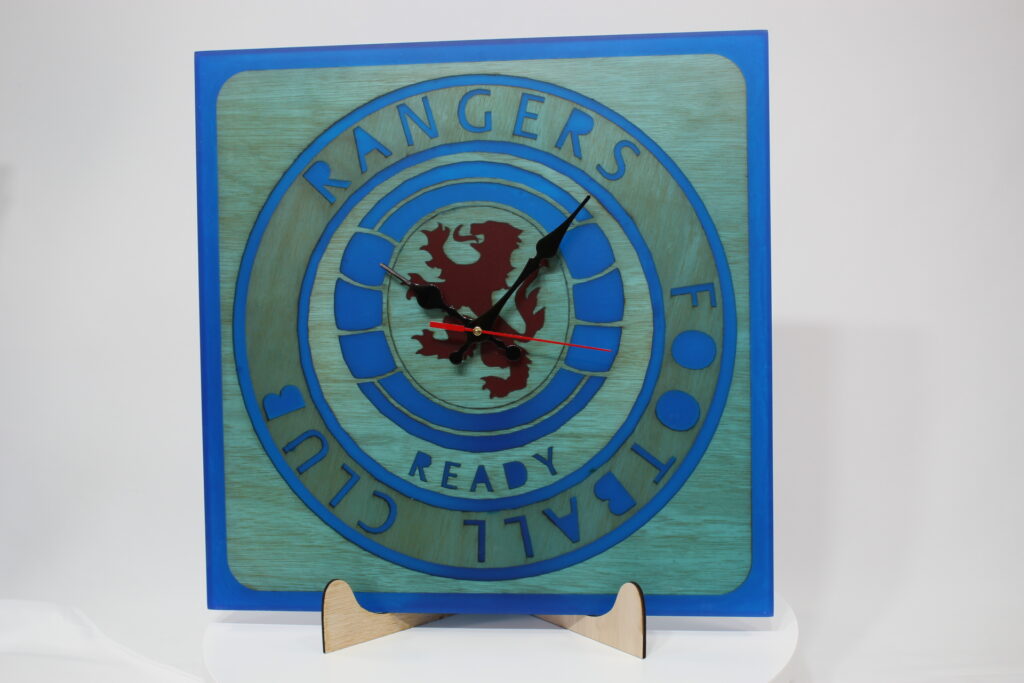 A square large wall clock made of epoxy resin blue and red with black hands indicators.