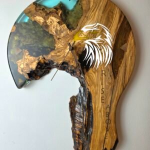 Round wall clock with natural olive wood grain and turquoise resin accent, featuring a white stylized bird feather design and black clock hands.