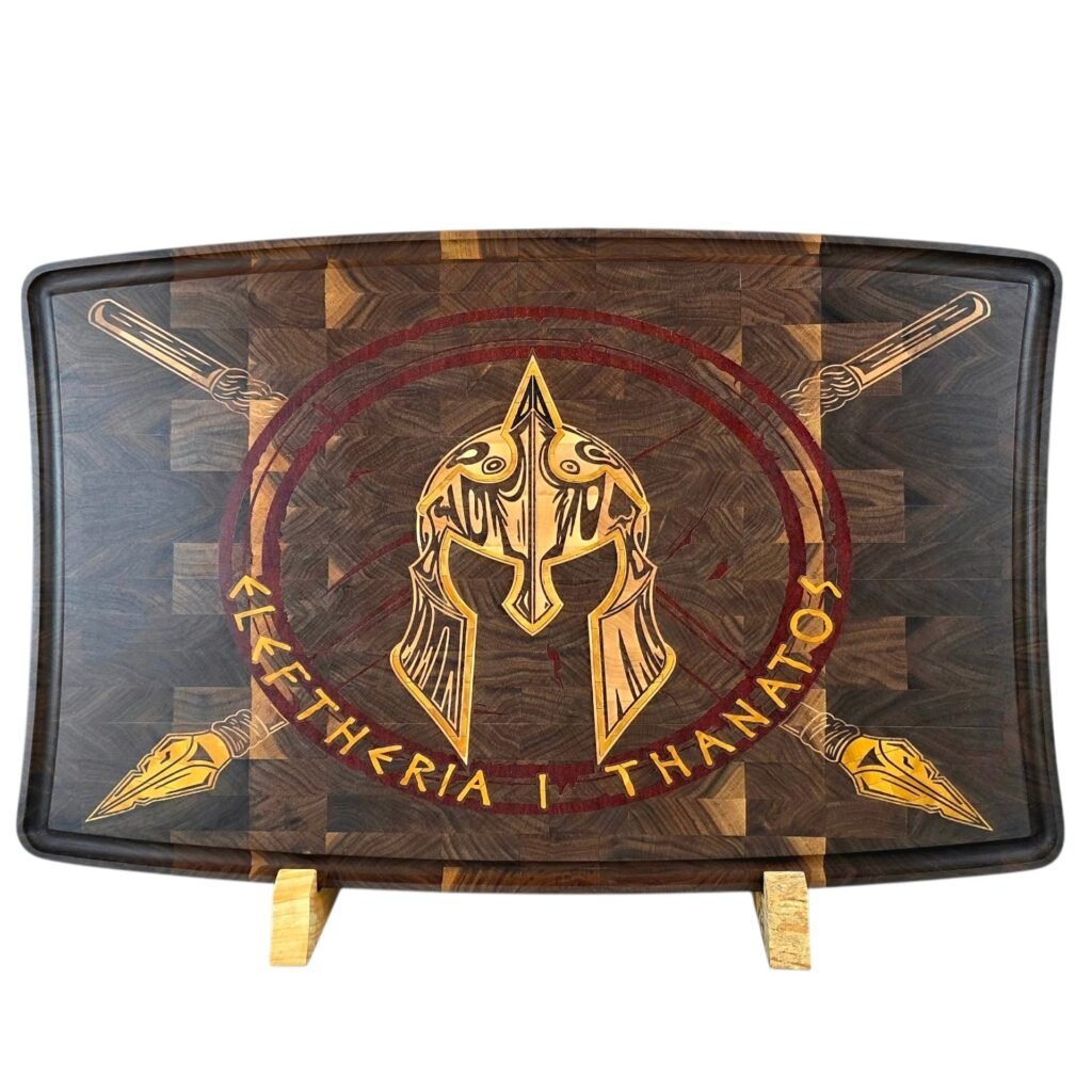 Spartan Helmet Inlay End-Grain Cutting Board - M & B CRAFT - M & B CRAFT Decorative wooden shield graphic with a golden helmet emblem and crossed spears, surrounded by circular text.