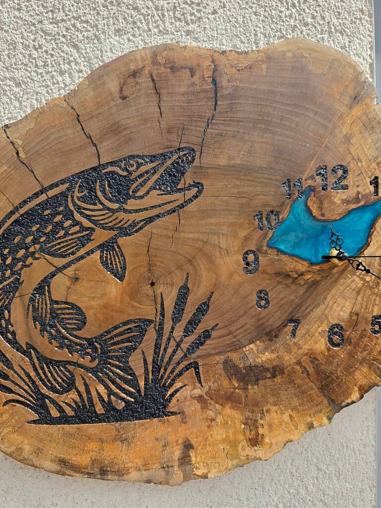 20260728_112032 - M & B CRAFT Decorative wooden slice with a black carved fish design and blue water, numbered marks around the edge, mounted on a rough wall.