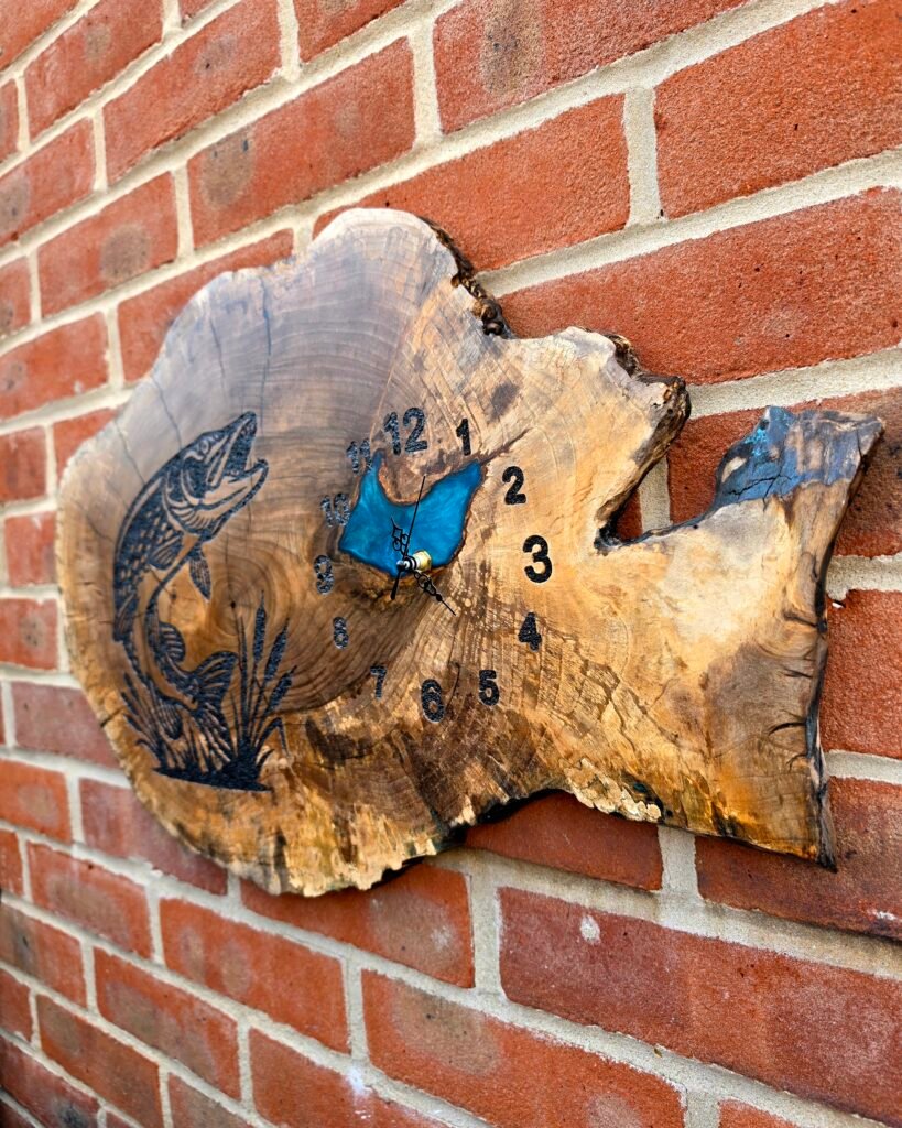 20260728_112221 - M & B CRAFT A round wooden tree-slice acting as a clock face with painted numbers, mounted on a red brick wall