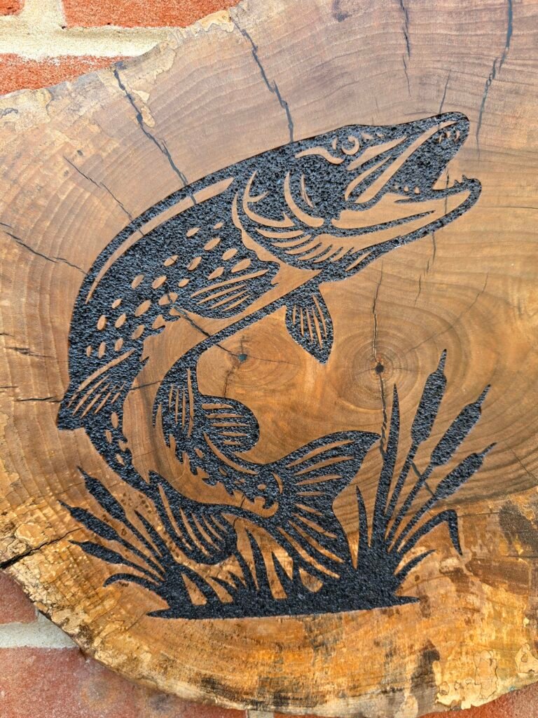 20260728_112237 - M & B CRAFT Carved black fish silhouette etched into a circular cross-section of a tree trunk, showing growth rings and cracks in the wood.